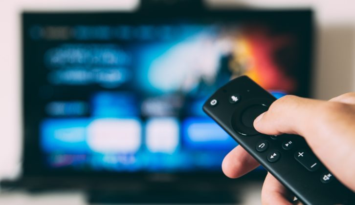 A hand holding a remote control points to a TV with a streaming service on display