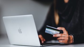 A person holds a credit card as they use a laptop.