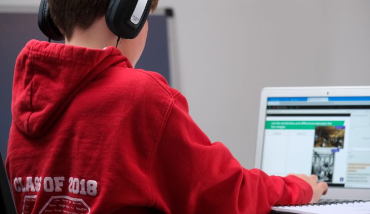 Young student wearing headphones working on computer. Digital learning