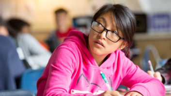 Hispanic girl writing in a notebook looking over her shoulder in the classroom - for bilingual education article.