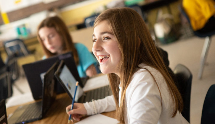 Smiling middle-school female student at table with other student in background for article on student choice