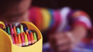 Closeup of box of crayons with blurry child in background for early education article