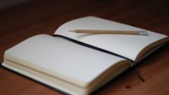 Blank journal open with pencil atop, sitting on a wood table for article on energizing "spa days"