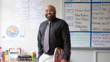 Black male teacher holding book at his side and smiling in classroom for teacher coaching cycle article