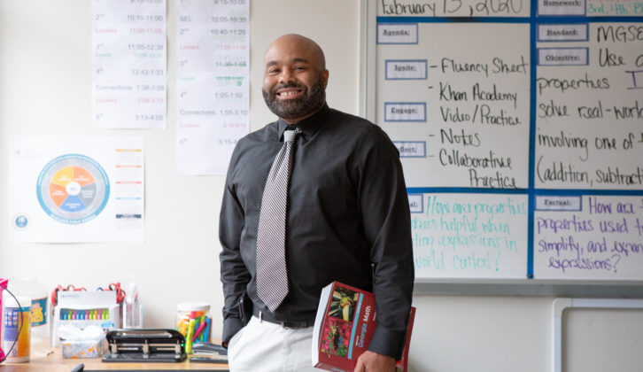 Black male teacher holding book at his side and smiling in classroom for teacher coaching cycle article