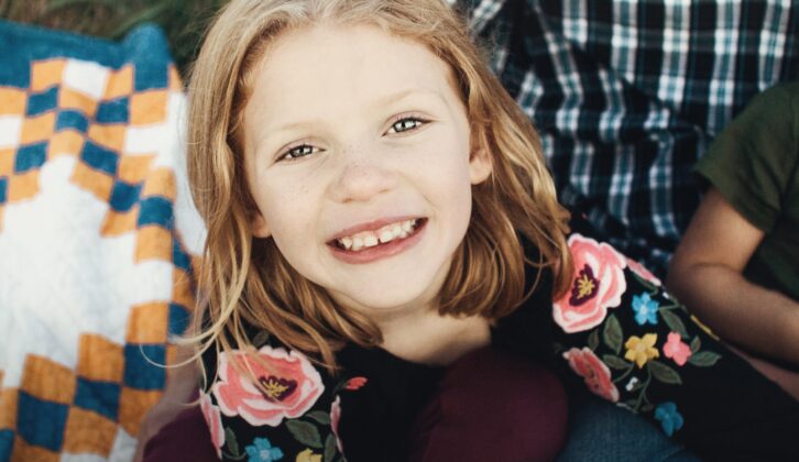Picture of red-headed young girl smiling with two flowers for article on shortage of speech-language pathologists