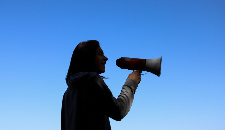 silhouette of woman holding megaphone against blue sky for article on how to consolidate communications in a district