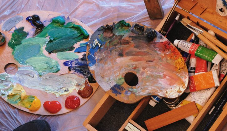 2 palettes with messy paint and brushes for article on teachers as artists and autonomy and creativity