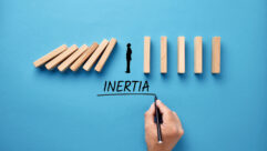 Businessman hand writing the word inertia with silhouette of a man standing against collapsing wooden dominos. Business inaction, apathy or inactivity concept. for article on executive team