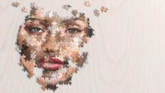 A close up image of a partly assembled jigsaw puzzle of a generic female face made of many different ethnicities and skin colours. The puzzle is on a light plain wooden surface, and shot with shallow depth of field with focus on the eyes for article on blending subjects.