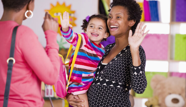 Teacher holding preschool child and waving goodbye to mom for article on bond between school and families