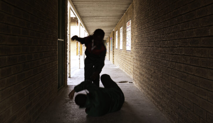 Two school kids fight in a dark passageway of their school, almost silhouette, for article on school safety measures