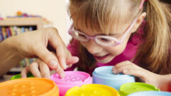 Little girl with poor vision is playing with colorful tactile toy cups as a part of occupational therapy with her teacher. for article on occupational therapist shortage