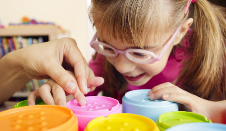 Little girl with poor vision is playing with colorful tactile toy cups as a part of occupational therapy with her teacher. for article on occupational therapist shortage