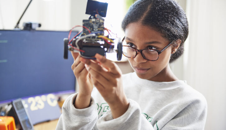 Black teenage girl with glasses holding up robot-like piece of technology for article on embrace tech