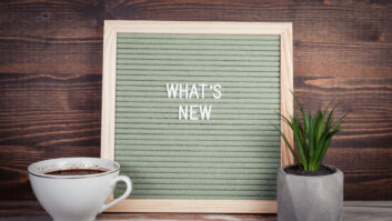 Sign board with removable white letters spelling out "What's New" next to coffee cup and potted plant for article on new experiences.