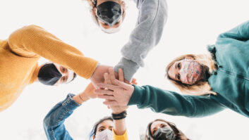 Millennial friends stacking hands together - View from below. They are wearing protective face masks. for teaching life skills story