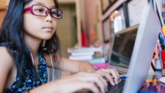 Young girl with glasses typing on laptop on a desk for article on virtual learning