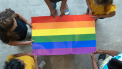 Children standing in a circle holding the edges of a flat rainbow flag