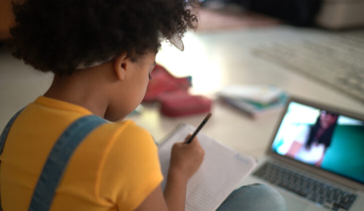 Rear view of a elementary age girl studying watching online classes for article on virtual tutoring
