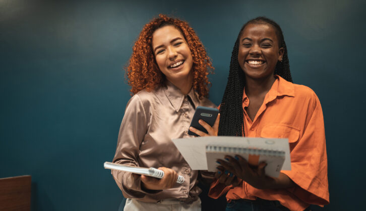 Young women with notebooks and papers, standing together and smiling