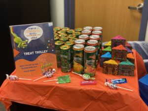 Treat Trolley for teachers: a small table with orange tablecloth covered with cans of Perrier, boxes of tea bags and other goodies- for Spangler story on gratitude